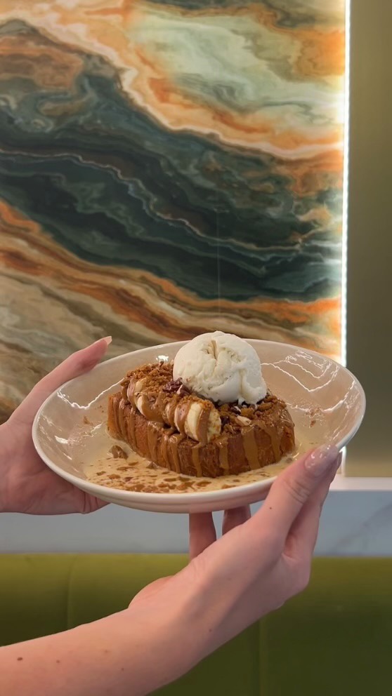 Dessert in a round metal tin with pistachio crumble and a gold spoon